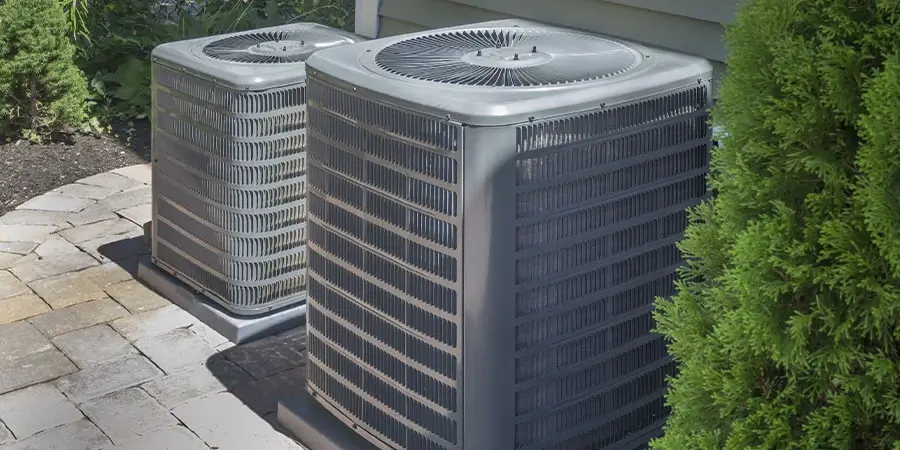 Two air conditioning units outside a house, surrounded by greenery.